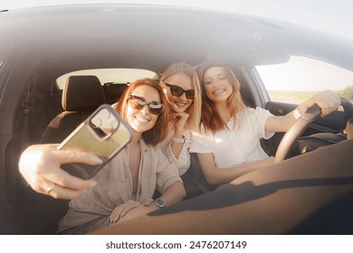 Three friends capturing memories with a selfie during a joyous car ride on a sunny day, portraying friendship and travel. - Powered by Shutterstock