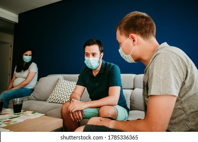 
Three Friends Chatting Together On The Sofa At Home. They Wear A Surgical Mask To Take Care Of The Covid 19 During The Pandemic. Social Distance