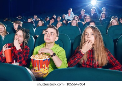 Three Friends Eating Popcorn By Watching Movie. Girl Drinking Fizzy Drink From The Big Red Can. Children Watching New Film Or Cartoon. Looking Interested And Exited. Wearing Colorful Shirts.