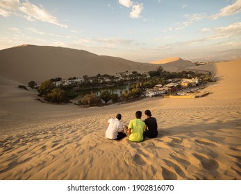 Three friends enjoying panoramic postcard view of Huacachina oasis town village desert sand dunes Ica Peru South America