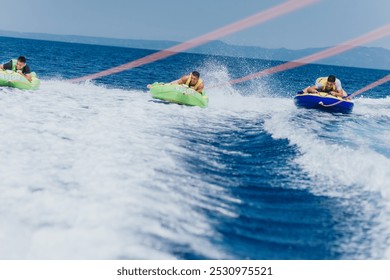 Three friends enjoying speedboat tubing on a sunny day in the sea, experiencing thrill and adventure. - Powered by Shutterstock