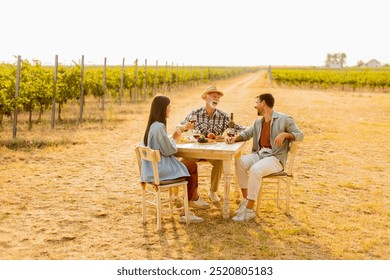 Three friends gather around a rustic table in a vineyard, enjoying wine, fresh fruits, and each other's company on a sunny day filled with joy and laughter - Powered by Shutterstock