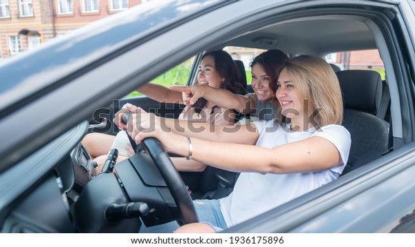 Three friends go on a trip.\
Caucasian women drive in a car and point fingers in\
surprise.