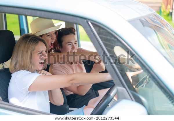 Three friends go on a trip.\
Caucasian women drive in a car and point fingers in\
surprise.