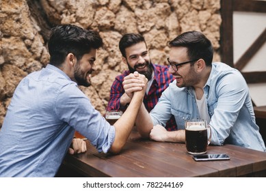 Three friends hand wrestle at the pub. - Powered by Shutterstock