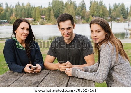 Three friends hanging out at a park with cell phones