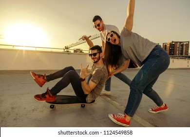 Three friends having fun while guy sitting on skateboard at sunset