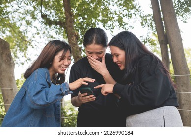 Three Friends Laugh And Giggle Over A Funny Video Playing On Their Cellphone While At The Park.