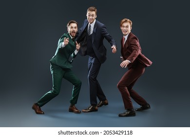 Three Friends. Men's Fashion. Three Handsome Men Friends In Elegant Suits Pose Together Fooling Around And Laughing. Dark Blue Background.