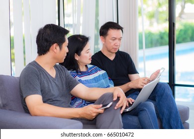 Three Friends On Line With Multiple Devices And Talking Sitting On A Sofa In The Living Room In A House Interior.