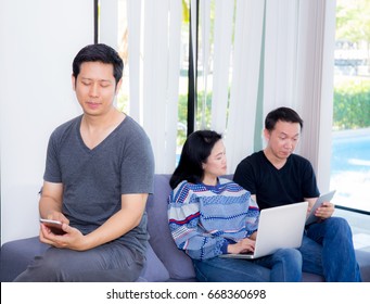 Three Friends On Line With Multiple Devices And Talking Sitting On A Sofa In The Living Room In A House Interior.