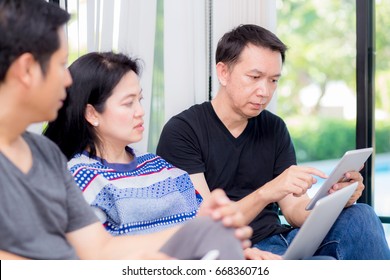 Three Friends On Line With Multiple Devices And Talking Sitting On A Sofa In The Living Room In A House Interior.