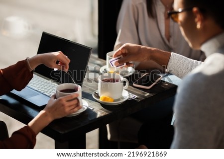 Three friends in a restaurant talking and having tea. Business colleagues in a meeting after work or during coffee break at a cafe bar. Abstract photo focus on tea cup