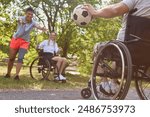 Three friends share laughter and fun in a park setting; one person who uses a wheelchair is playfully interacting with a soccer ball, demonstrating active and inclusive leisure activities.