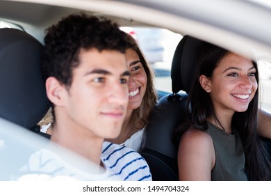 Three friends are sitting in a car, two in the front and one in the back and they are all laughing and smiling