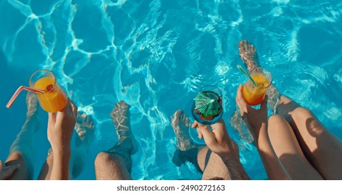 Three friends sitting on the edge of a pool with cocktails in their hands, top view - Powered by Shutterstock