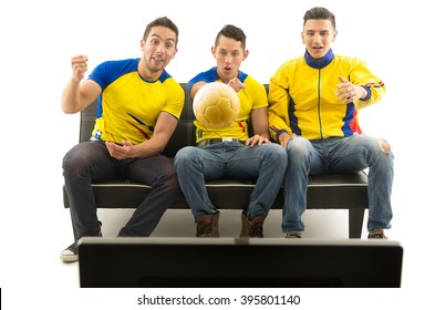 Three Friends Sitting On Sofa Wearing Yellow Sports Shirts Watching Television With Enthusiasm, Golden Ball Flying In Front, White Background, Shot From Behind Tv