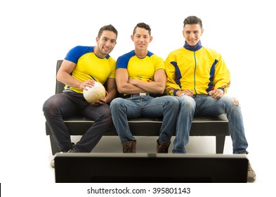 Three Friends Sitting On Sofa Wearing Yellow Sports Shirts Watching Television With Enthusiasm, White Background, Shot From Behind Tv