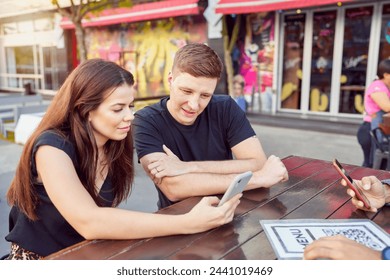 three friends sitting in an outdoor cafe looking at the menu with QR code - Powered by Shutterstock