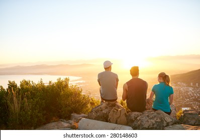 Three Friends Watching The Sunrise Over The City Together From A Mountain Nature Trail 