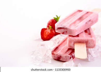 Three frozen popsicles with fresh strawberry ingredients stacked chilling on a bed of crushed ice with copy space alongside - Powered by Shutterstock