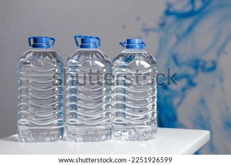 Three full 5 liter bottles of water on a white table on a gray background. Water delivery