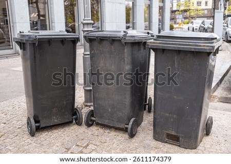 Three garbage cans are on the sidewalk
