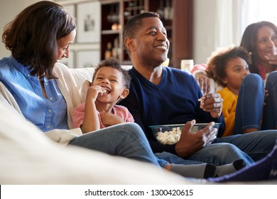 Three generation African American family family sitting on the sofa in living room, watching TV and eating popcorn, selective focus