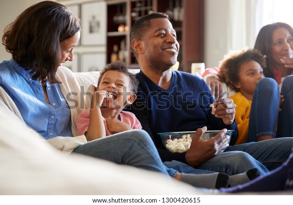 Three generation African American family family\
sitting on the sofa in living room, watching TV and eating popcorn,\
selective focus