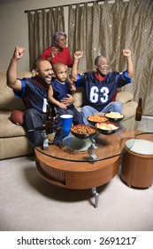 A Three Generation African-American Family Cheering And Watching Football Game Together On Tv.