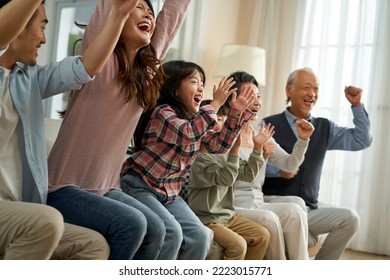 three generation asian family sitting on couch at home watching live broadcasting of soccer games on TV - Powered by Shutterstock