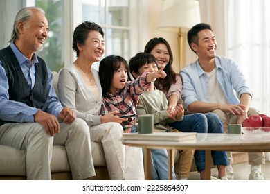 three generation asian family sitting on couch at home watching tv together happy and smiling - Powered by Shutterstock
