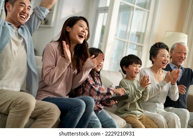 three generation asian family sitting on couch at home watching tv together happy and excited - Powered by Shutterstock