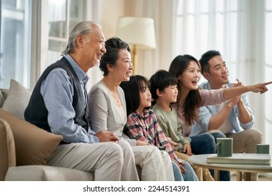 three generation asian family sitting on couch at home watching tv together happy and smiling - Powered by Shutterstock