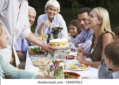 Three Generation Family Celebrating Birthday Of Woman At Dining Table Outdoors