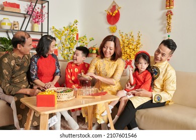 Three generation family celebrating Tet at home, talking and enjoying tea with candied fruits - Powered by Shutterstock