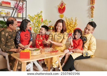 Three generation family celebrating Tet at home, talking and enjoying tea with candied fruits