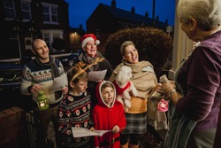 Three Generation Family Are Doing Door-to-door Carol Singing. There Is A Senior Woman At The Door, Appreciating Their Singing.