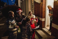 Three Generation Family Are Doing Door-to-door Carol Singing. There Is A Senior Woman At The Door, Appreciating Their Singing.