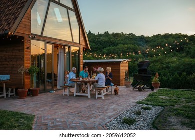 Drei Generationen Familie mit einer Gartenparty im Sommer. Sie sitzen am Esstisch im Garten und essen zu Abend