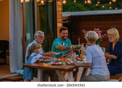 Three generation family having a garden party in the summer. They are sitting at the dining table in the backyard and having dinner - Powered by Shutterstock