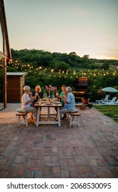 Three Generation Family Having A Garden Party In The Summer. They Are Sitting At The Dining Table In The Backyard And Having Dinner