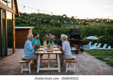 Drei Generationen Familie mit einer Gartenparty im Sommer. Sie sitzen am Esstisch im Garten und essen zu Abend