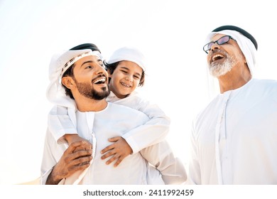 Three generation family making a safari in the desert of Dubai wearing white kandura outfit. Grandfather, son and grandson spending time together in the nature. - Powered by Shutterstock