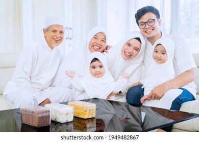 Three Generation Happy Muslim Family Smiling At The Camera While Sitting Together On The Couch In The Living Room. Shot At Home