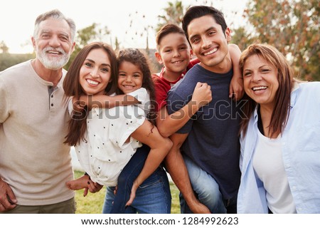 Three generation Hispanic family standing in the park, smiling to camera, selective focus