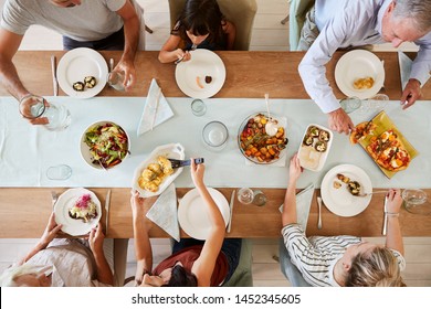 Three Generation White Family Sitting At A Dinner Table Together Serving A Meal, Overhead View