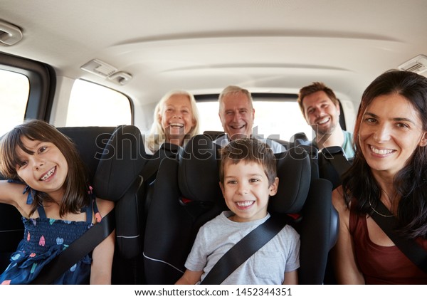 Three generation white family
sitting in two rows of passenger seats in a car, smiling to
camera