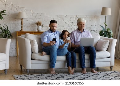 Three Generational Family, Old Hoary Man, His Grown Up Son And Little Grandson Sit On Couch At Home With Diverse Modern Gadgets, Use Application, Surfing Internet, Ignoring Each Other. Overuse Concept