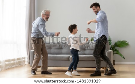 Three generations of active men dancing in living room little boy enjoy time with elderly grandfather and young father, concept of warm relations, understanding, best friends, intergenerational family
